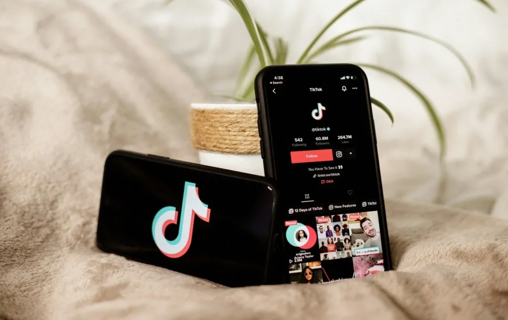 Два смартфона с TikTok на бежевой ткани рядом с растением в горшке