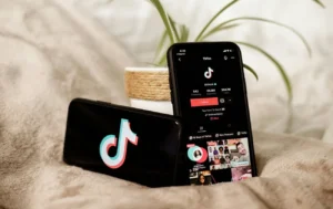 Два смартфона с TikTok на бежевой ткани рядом с растением в горшке