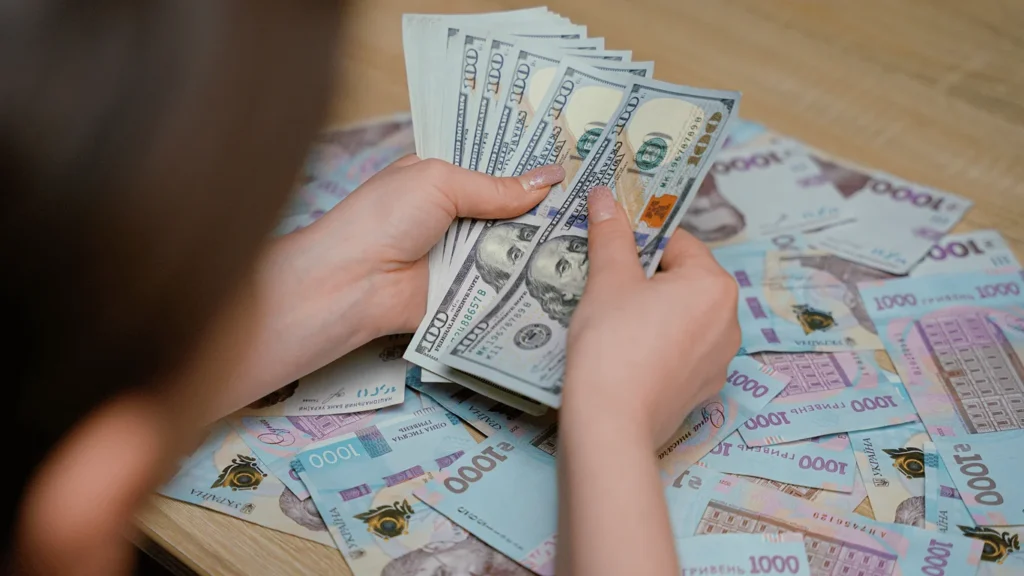 Руки перераховують пачки по 100 доларів серед українських гривень 1000 грн