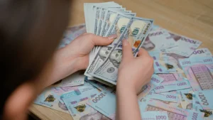 Руки перераховують пачки по 100 доларів серед українських гривень 1000 грн