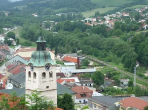 Вид на церковну вежу з годинниками в польському містечку на тлі зелених пагорбів і залізничних колій, що ілюструє контекст діалогу Польщі та України.