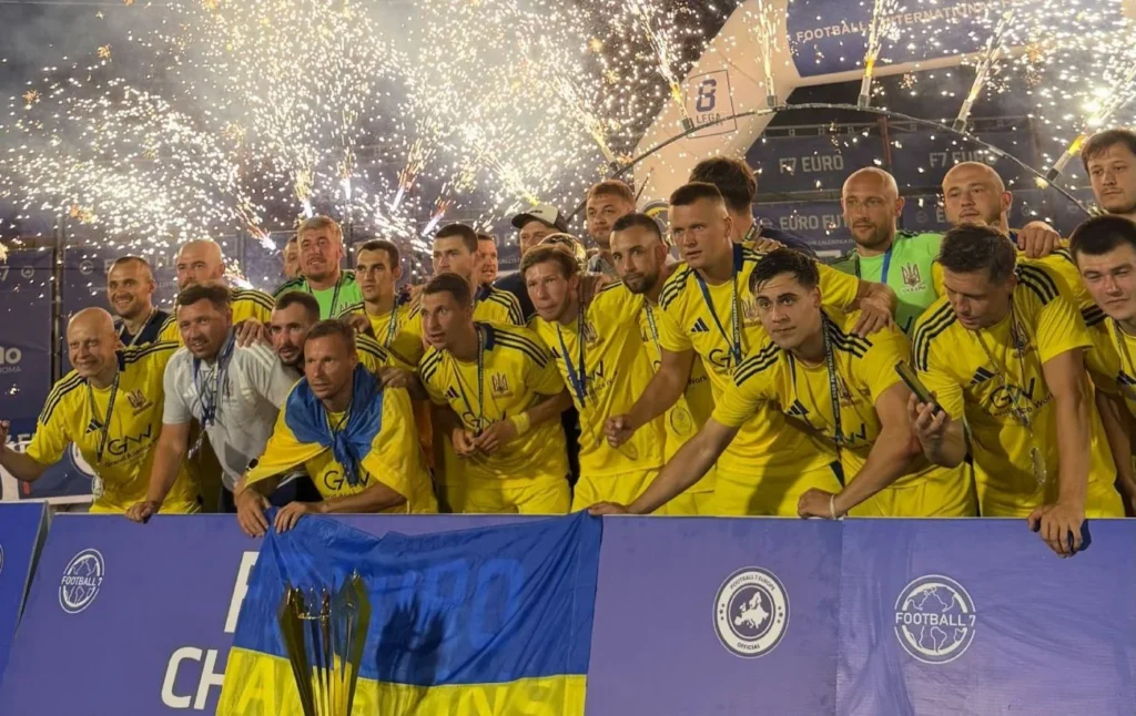 Игроки сборной Украины по футболу 7х7 празднуют победу с кубком и флагом под фейерверками