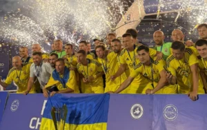 Игроки сборной Украины по футболу 7х7 празднуют победу с кубком и флагом под фейерверками