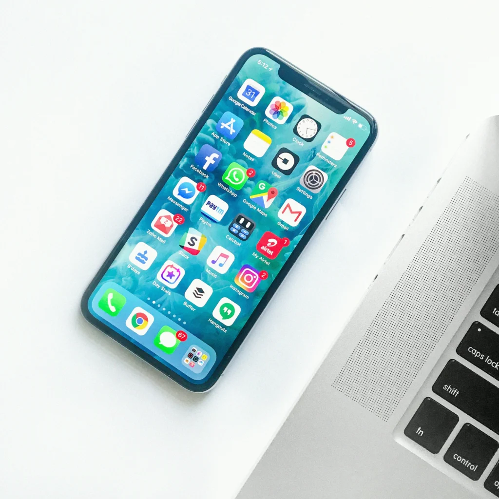 iPhone з відкритим екраном додатків лежить біля клавіатури MacBook на білому столі