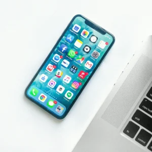 iPhone з відкритим екраном додатків лежить біля клавіатури MacBook на білому столі
