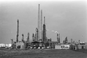 Чорно-біле фото нафтопереробного заводу з високими трубами, резервуарами та автомобілями