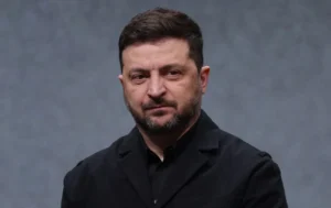 Володимир Зеленський у чорному костюмі на сірому фоні дивиться вбік